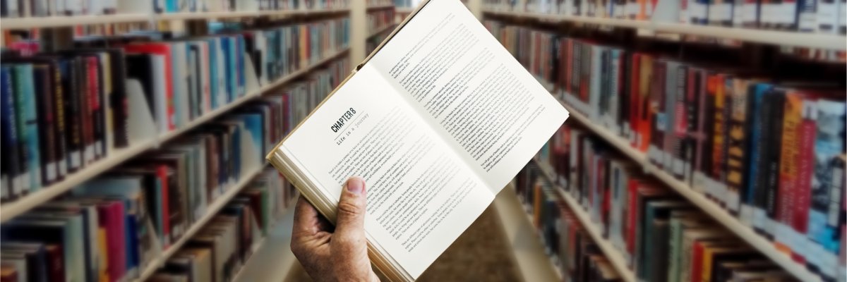 Person hält Buch hoch zwischen Bücherregalen