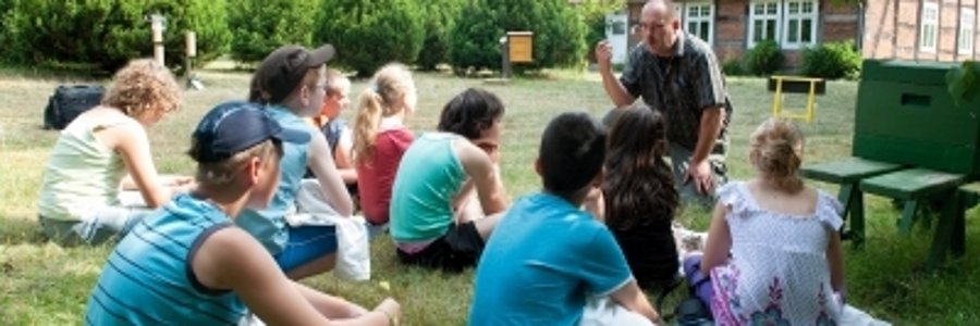 eine Gruppe jugendlicher sitzt auf dem Rasen und hört einem Vortragenden zu