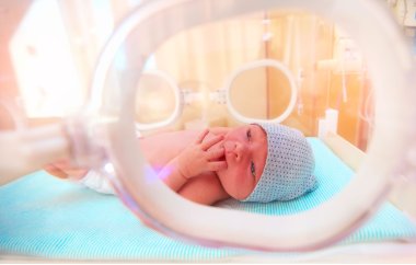 Neugeborenes Baby liegt im Säuglingsinkubator im Krankenhaus und lutscht an den Fingern Neugeborenes Baby liegt im Säuglingsinkubator im Krankenhaus und lutscht an den Fingern