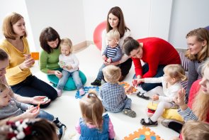 Kinder mit Müttern sitzen im Kreis und lernen Farben, Zahlen und Figuren im Kindergarten