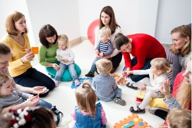 Junge Mütter mit kleinen Kindern beim Spielen Kinder mit Müttern sitzen im Kreis und lernen Farben, Zahlen und Figuren im Kindergarten