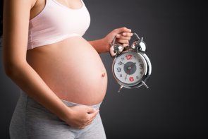 Abgeschnittenes Bild einer schwangeren Frau, die den Wecker in der Nähe hält