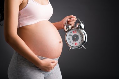 Abgeschnittenes Bild einer schwangeren Frau, die den Wecker in der Nähe hält