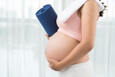 Aktive und sportliche Schwangerschaft Abgeschnittenes Bild einer sportlichen Schwangeren mit Yogamatte