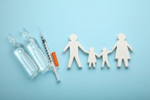 hellblauer Hintergrund, Spritze mit zwei Ampullen, Familiengruppe aus weißen Holz