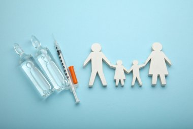hellblauer Hintergrund, Spritze mit zwei Ampullen, Familiengruppe aus weißen Holz