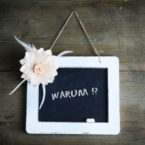 Holzwand mit weißer Tafel und Blumenornament, Aufschrift warum