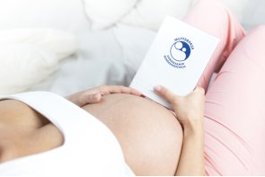 Schwangere Frau liegend hält  Babybauch und Mutterpass