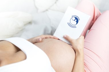 Schwangere Frau liegend hält  Babybauch und Mutterpass