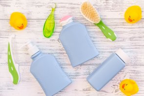 blaue Fläschen für die Kinderpflege, Kamm und Bürsten in grün, gelbe Gummiente auf grauem Holzhintergrund,