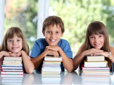 3 Kinder stützen sich auf ihren Buchstapel ab