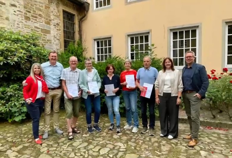 eine Gruppe von Personen bei der Übergabe von Urkunden im Innenhof eines mittelalterlichen Gebäudes