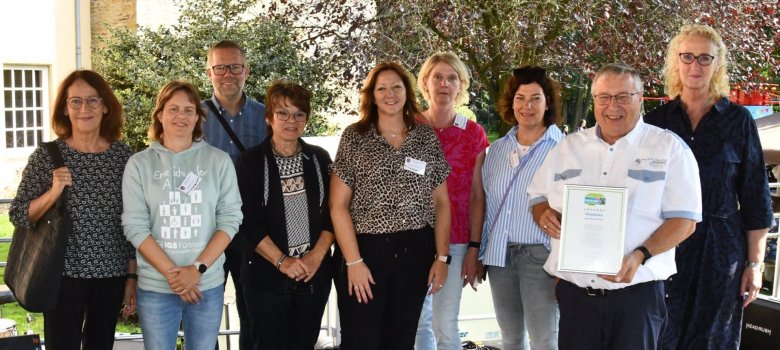 Übergabe der Urkunde mehrere Personen stehen auf einer Bühne bei der Übergabe einer Urkunde