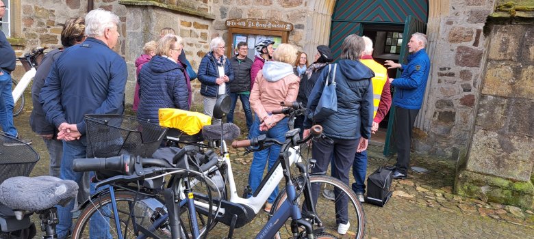 Eine kleine Gruppe steht mit ihren Fahrrädern vor dem Eingang einer Kirche