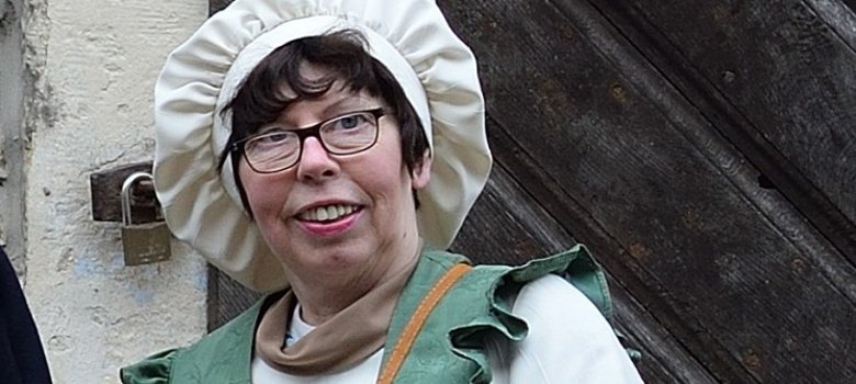 Frau in Kostüm steht mit Korb vor altem Gebäude